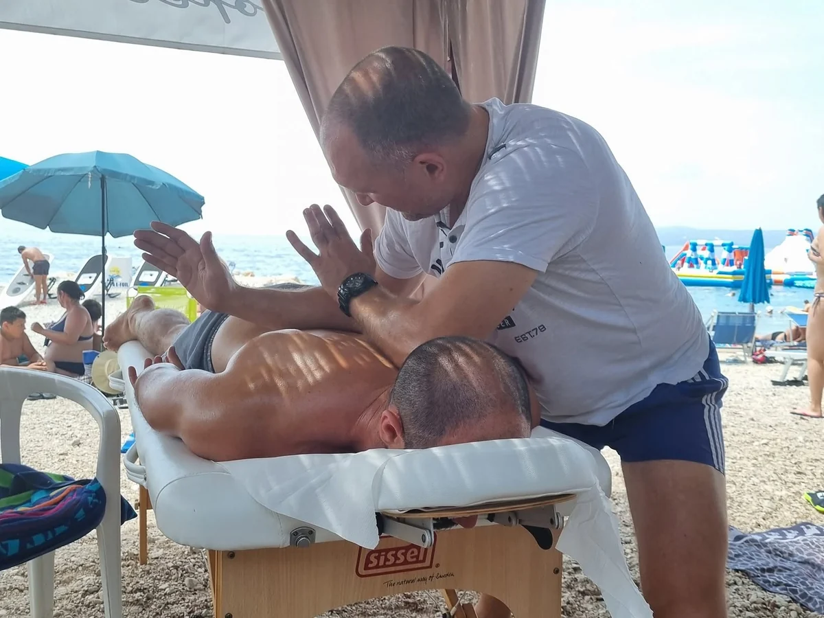 A therapist massages the back of a guest lying on a massage table by the sea in Makarska.