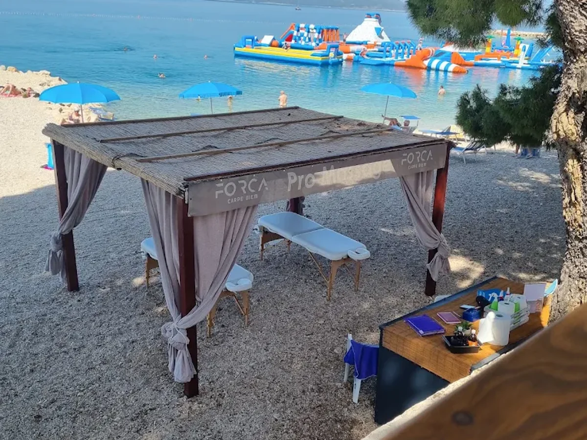 FORCA canopy with a massage table on a pebble beach in Makarska, beside the sea and pine trees.